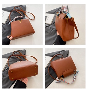 Detailed view of brown leather handbag, featuring stylish metal V logo, handle silk scarf.