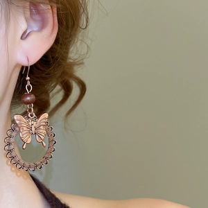 Detail of vintage bronze butterfly earrings with wooden beads on model ear
