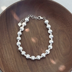 Detail of S925 silver beaded bracelet with heart pendant on dark wooden tray