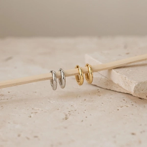 Classic silver and gold stainless steel hoop earrings on a minimalist wooden display