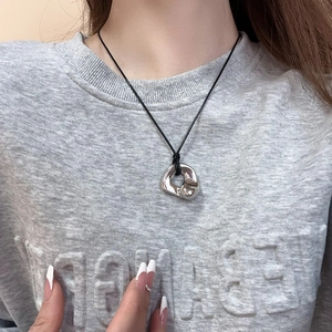 Close-up of silver irregular liquid metal pendant on black cord necklace worn by model