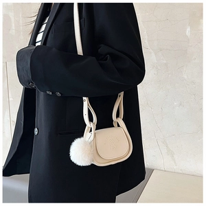 Detail of cream mini saddle bag with cat embossing and detachable white pompom charm