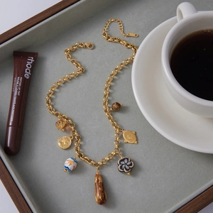 Detail of gold titanium steel necklace with resin charms and ceramic beads in a tray