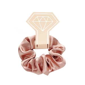 Detail of rose gold satin scrunchie showing glossy fabric texture on a diamond card