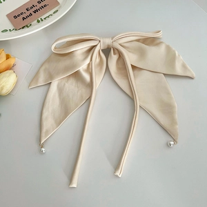Detail of beige satin bow hair clip with long ribbons and delicate pearl pendants