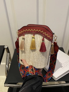 Detail of beige straw bucket bag featuring red leather trim and colorful tassel charms