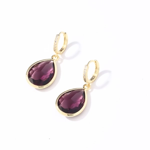 Detail of gold earrings featuring purple teardrop crystals and sparkling zircon accents