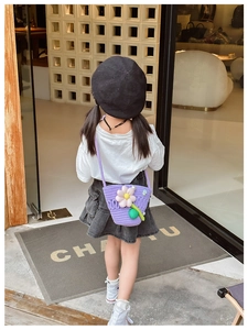 Detail of a purple woven crossbody bag for kids featuring a large white flower and strap
