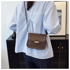 Détail d'un sac bandoulière en cuir marron avec fermoir doré porté par un mannequin
