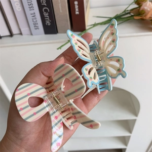 Detail of blue butterfly hair claw clip with pink strawberry pattern held by hand