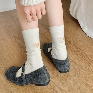 Detail of white cotton socks with Follow Your Heart embroidery on a wooden floor