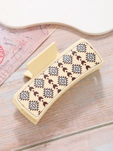 Detail of cream shark hair clip featuring ethnic geometric patterns on a wooden surface