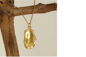 Close-up of a gold irregular organic pendant necklace on a natural wood stand