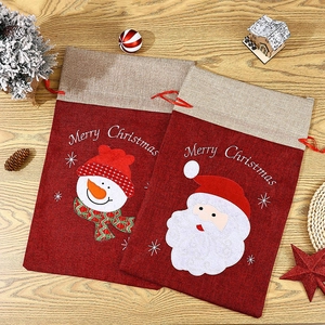 Close-up of burlap Christmas gift bags with Santa and Snowman prints on wood background