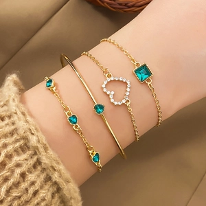Detailed close-up of golden bracelets set featuring emerald green gems and heart charms