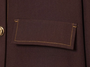 Close-up of contrast stitching on lapel jacket pocket with a gold button detail