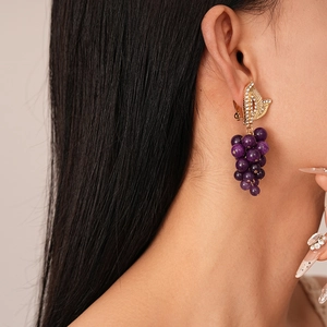 Détail de boucles d'oreilles en forme de raisin avec perles mauves et feuilles dorées