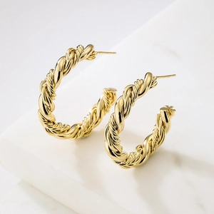 Minimalist gold plated twisted C-shaped hoop earrings on white marble background