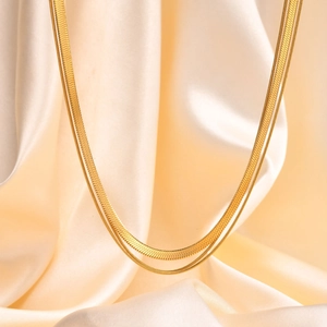 Detail of golden double-layered snake bone chain necklace on cream silk fabric background