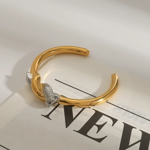 Close-up of two-tone gold and silver steel nail bracelet on a modern newsprint background