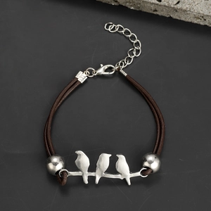 Detailed shot of handmade hummingbird bracelet with brown braided cord and silver bird accents