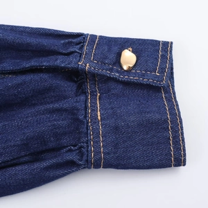 Détail du poignet en denim bleu foncé avec bouton doré et coutures jaunes apparentes