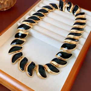 Détail d'un collier vintage doré avec feuilles en émail noir dans une boîte à bijoux