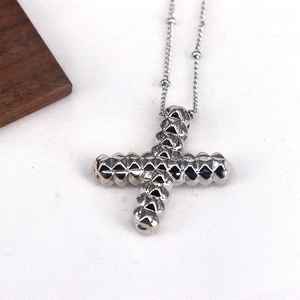 Close-up of a silver punk-style cross pendant with textured metal spike details