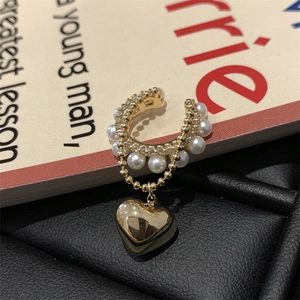 Dettaglio di un ear cuff dorato con perle bianche e ciondolo a cuore su sfondo materico