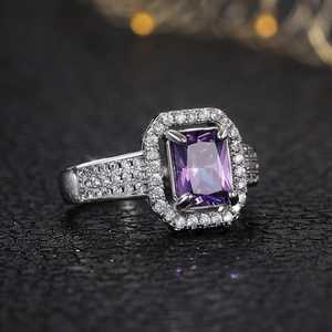 Macro side view of emerald-cut purple gemstone ring with halo diamond setting