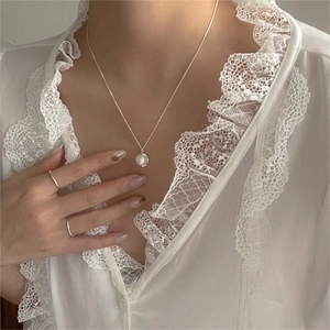 Detail of 925 silver necklace with pearl pendant and minimalist rings on female model