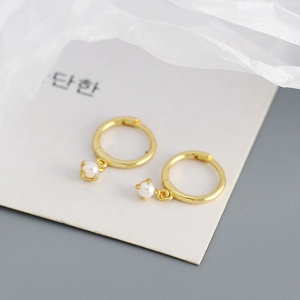 Macro view of gold hoop earrings with four-claw set faux pearls on a white surface