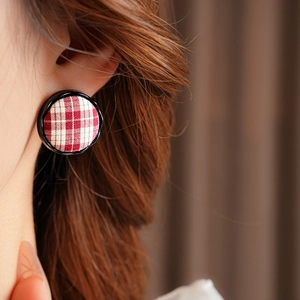 Close-up of a model wearing round red plaid fabric earrings with black trim