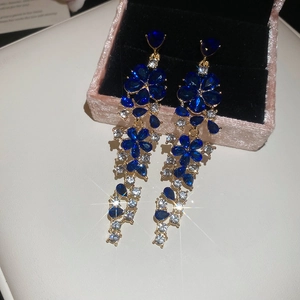 Close-up of gold drop earrings with blue and clear gems on pink velvet box