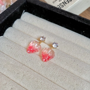 Macro detail of strawberry resin earrings with sparkling zircon studs on beige velvet base
