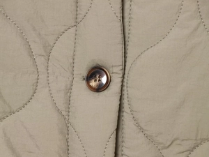 Close-up of khaki quilted leopard jacket showing resin button and curved stitching details