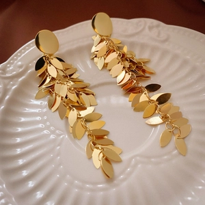 Detailed view of layered gold leaf sequin fringe earrings on a white shell plate
