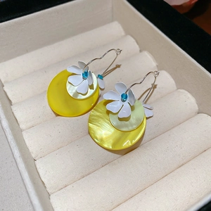 Detail of floral shell earrings with yellow and white petals on beige velvet