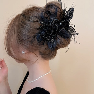 Close-up of black flower hair claw with elegant feathers, sequins and mesh on brown hair
