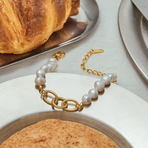 Baroque pearls and textured 18K gold stainless steel links on a decorative metal tray