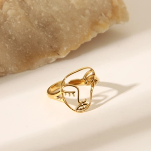 Bague au design de visage abstrait doré posée sur un support en pierre naturelle