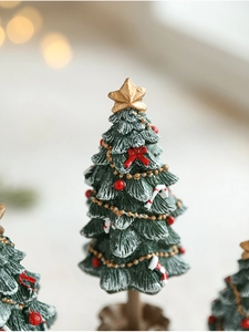 Close-up of mini green resin Christmas tree with red bows, gold star and snow texture