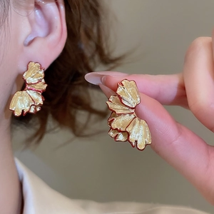 Detailed close-up of golden petal earrings with red trim and drop pearl accents