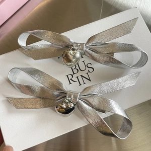 Silver bow hair clips with heart charms on white display card with metal background