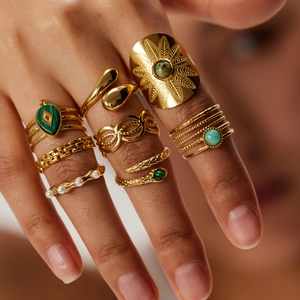 Detailed shot of gold woven rings featuring green natural stones and white pearls on hand