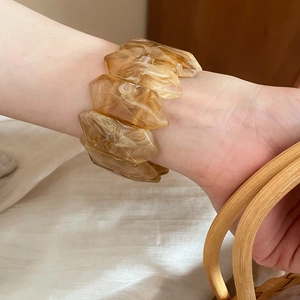 Detail of irregular marble textured resin bangle with amber tones on a female wrist