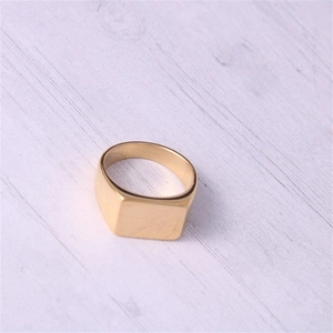 Detail van een vierkante gouden roestvrijstalen ring op een lichte houtnerf achtergrond