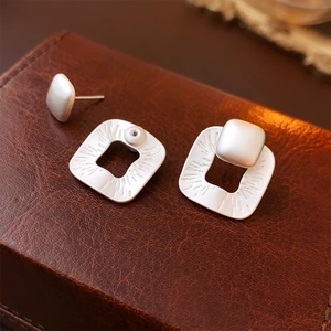 Detail of silver square earrings with pleated texture on premium brown leather