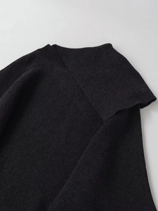 Detail of black wool asymmetric neckline and fine ribbed knit texture on the poncho top