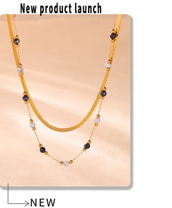 Close-up of double-layered gold snake chain necklace with black and white stone beads